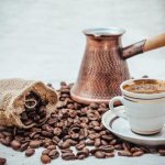 Чашка кофе на фоне турки и кофейных зерен