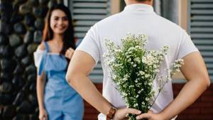 A man hides a bouquet from a girl standing in front of him